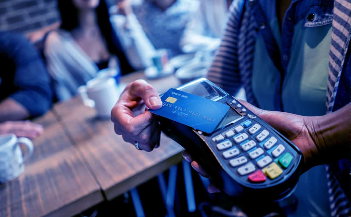 A person tapping their credit card on a card reader in a cafe