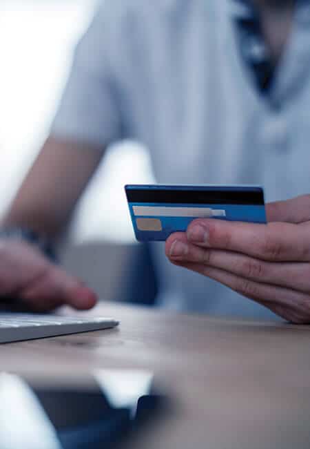 A man is holding his credit card in his hand typing the information into his laptop to complete a transaction. 